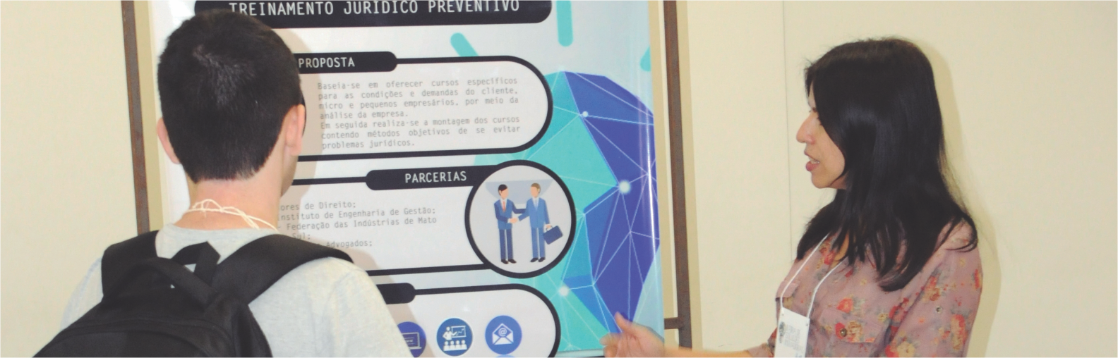 Duas pessoas na frente de um banner da feira.