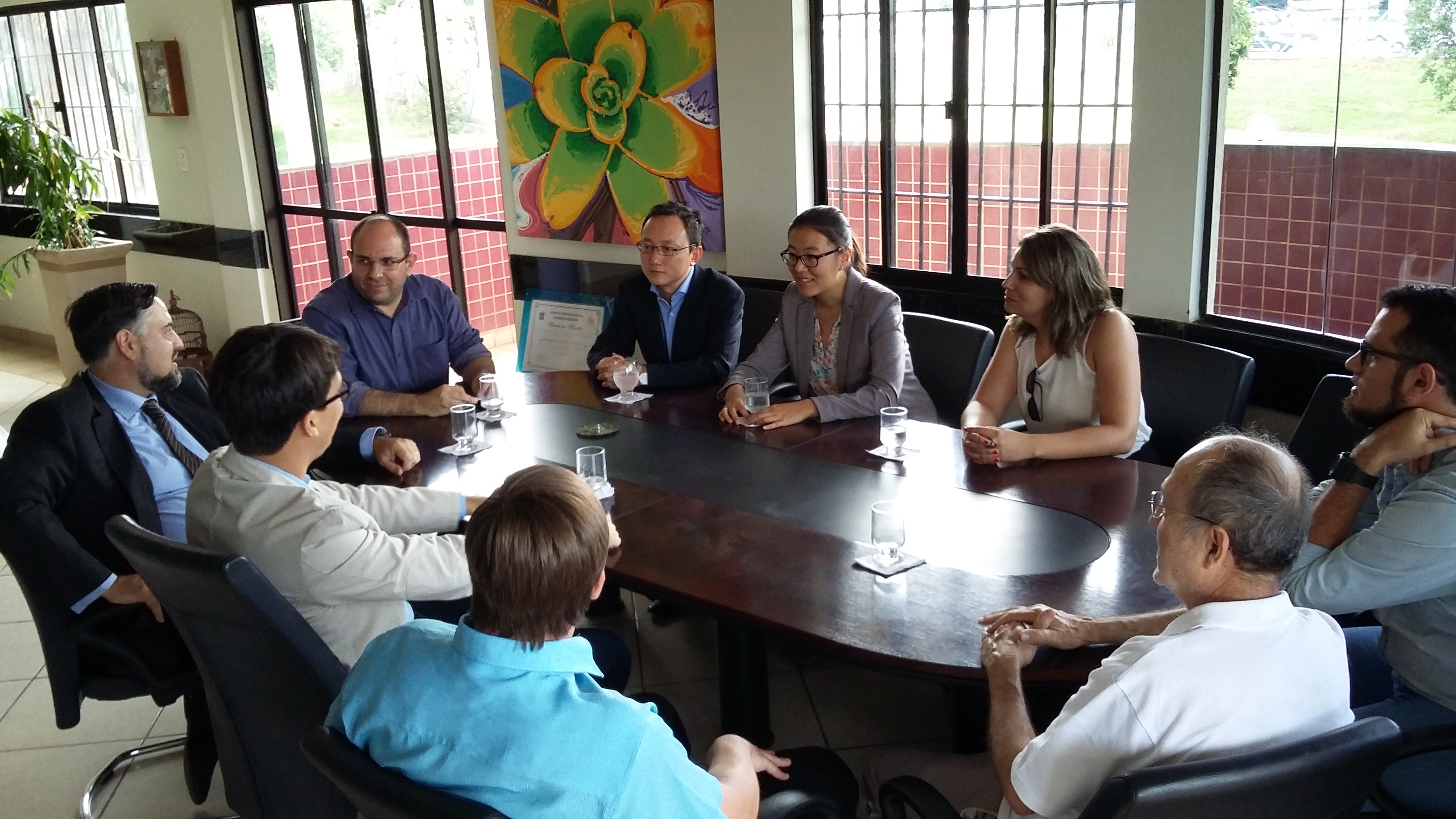 Imagem com o professor Marcelo Turine sentado em uma mesa rodeado por integrantes da Technische Universität Dresden (Alemanha), da Sanesul e professores da UFMS.